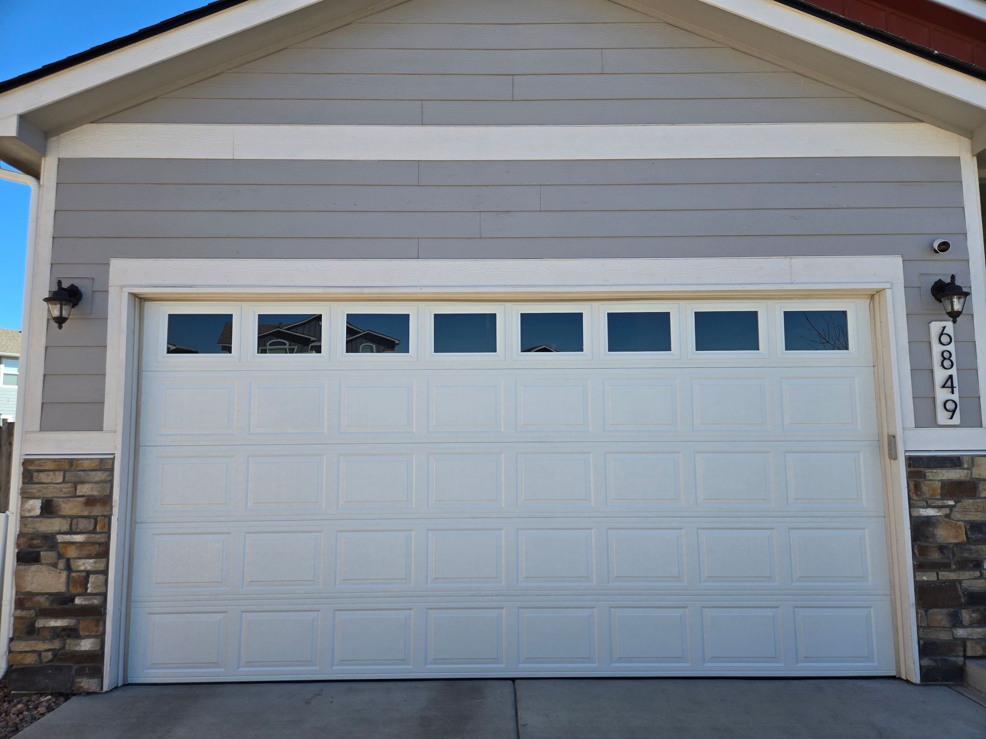 White garage door with windows, on a light gray house with stone accents.