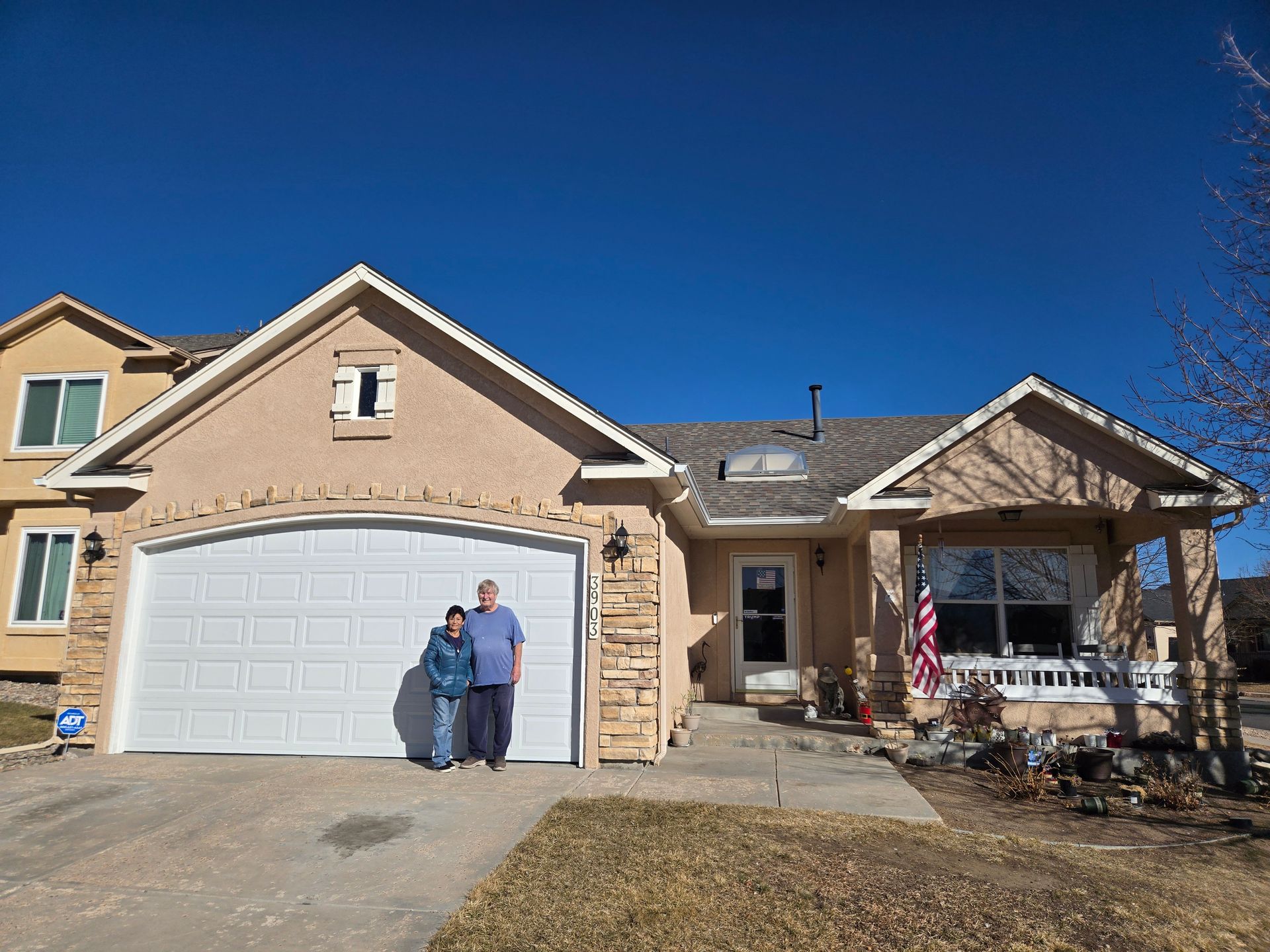Man and child standing in front of a tan house with a white garage door, blue sky.
