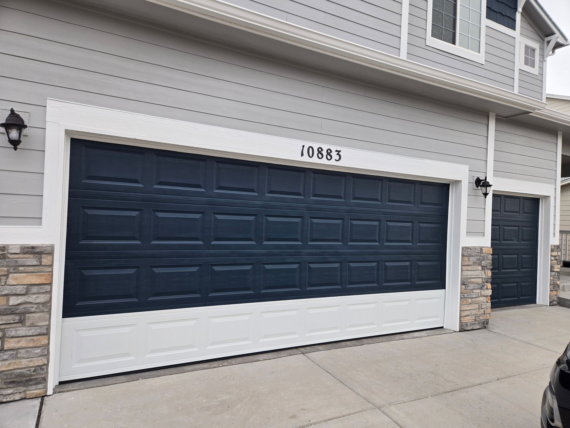 Garage doors of a house, dark blue with white trim, address 10443 above the main door.