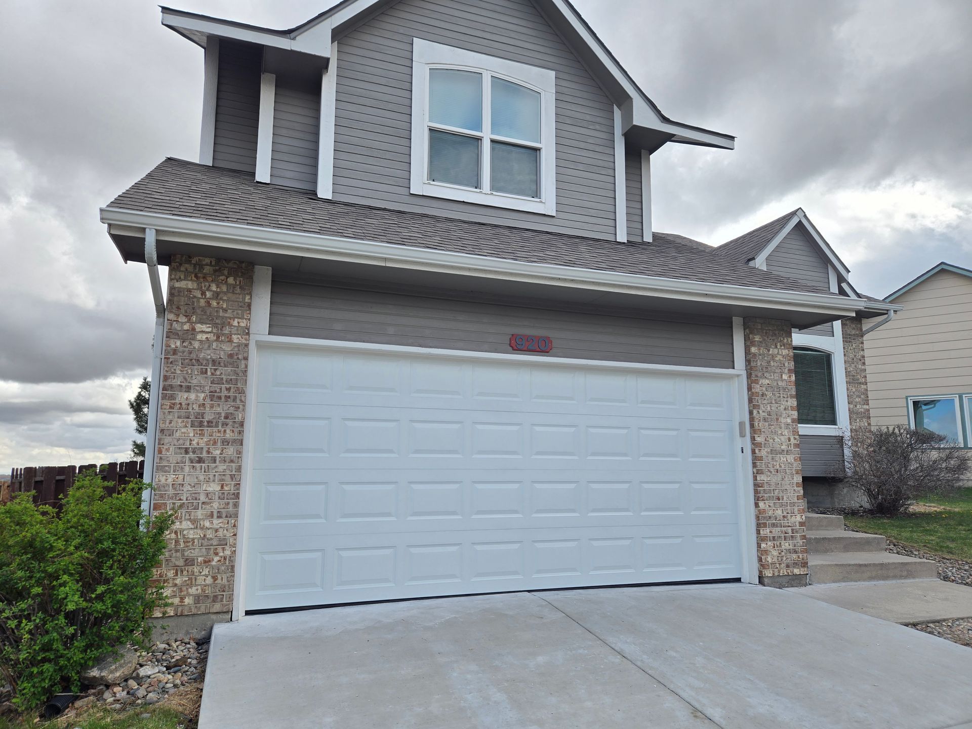 Two-story house with white garage door and gray siding, accented with brick.
