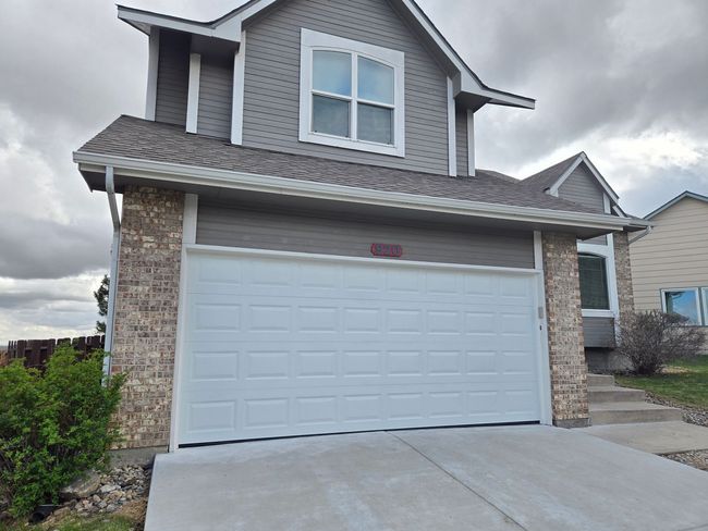Two-story house with white garage door and gray siding, accented with brick.