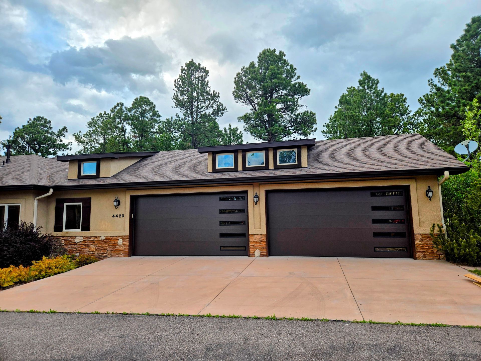 Tan stucco house with two dark brown garage doors, brown roof, and concrete driveway.