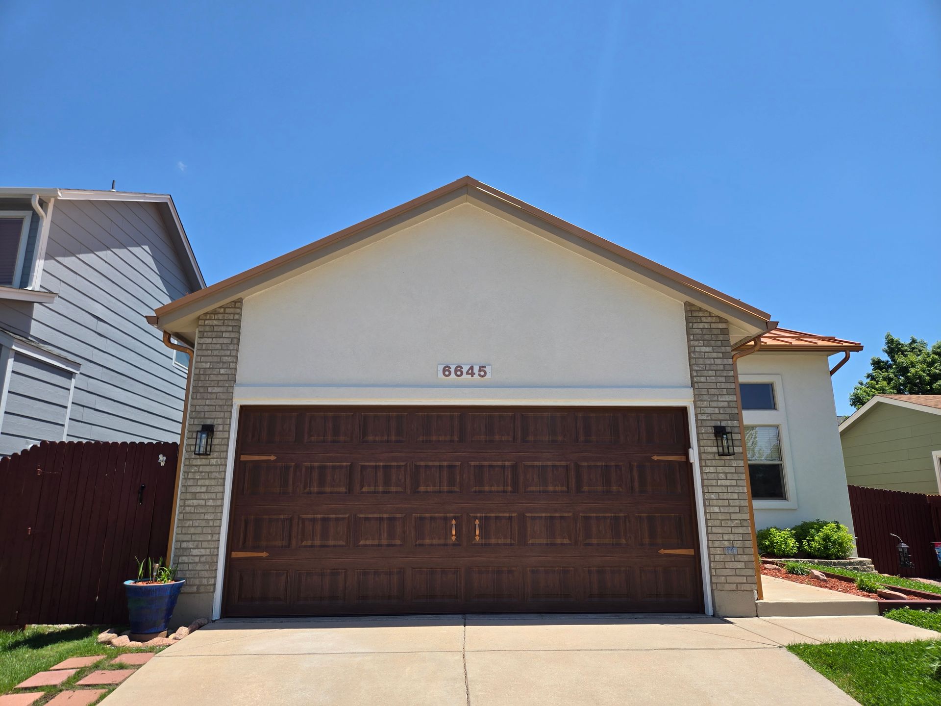 Brown garage door on a beige house with decorative brick accents and a clear blue sky.