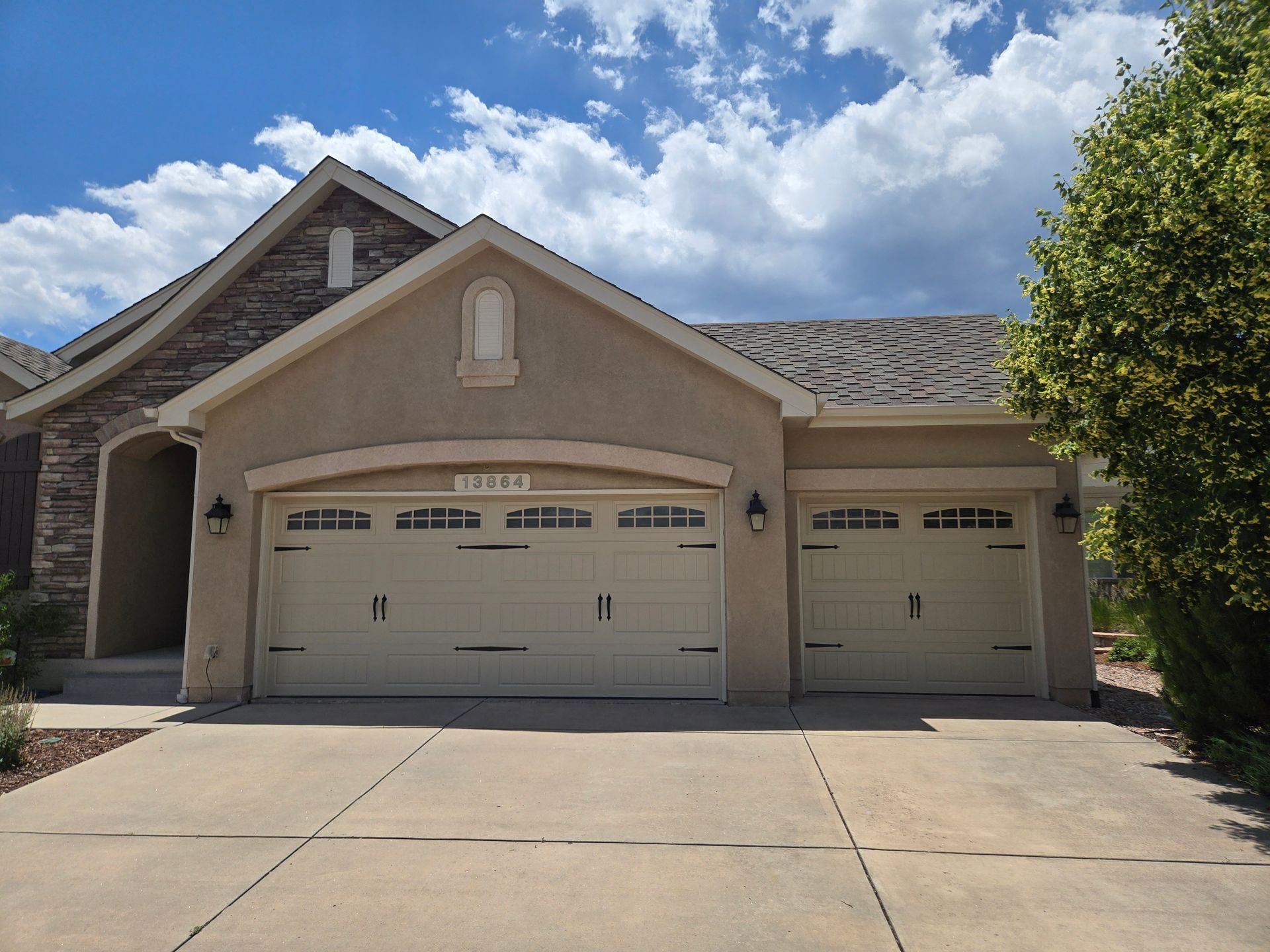 Tan stucco house with beige garage doors, concrete driveway, and blue sky.