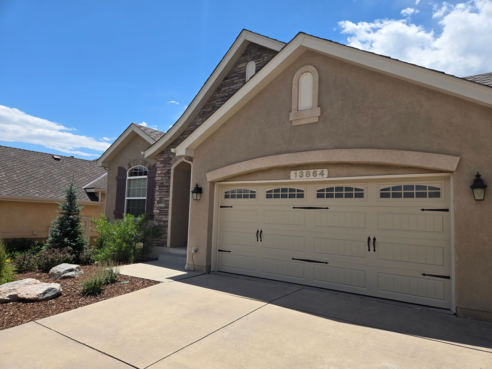 Tan stucco home with a two-car garage, stone accents, and a driveway, under a blue sky.