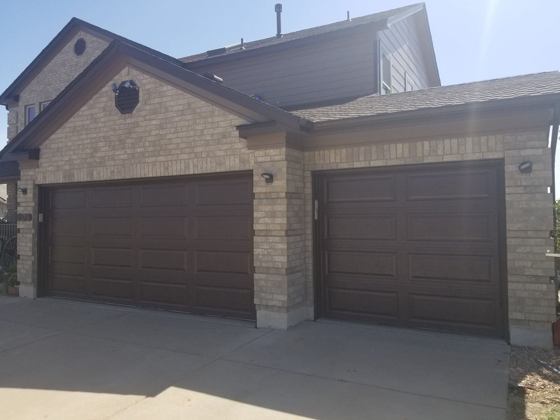 Brown garage doors on a two-story brick house with a concrete driveway.