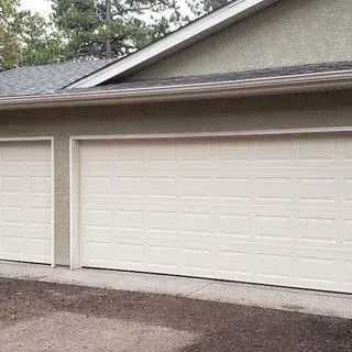 Two white garage doors on a light green building with a gray roof.