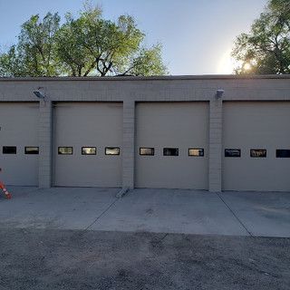 Three garage doors with windows in a beige building under a sunny sky.