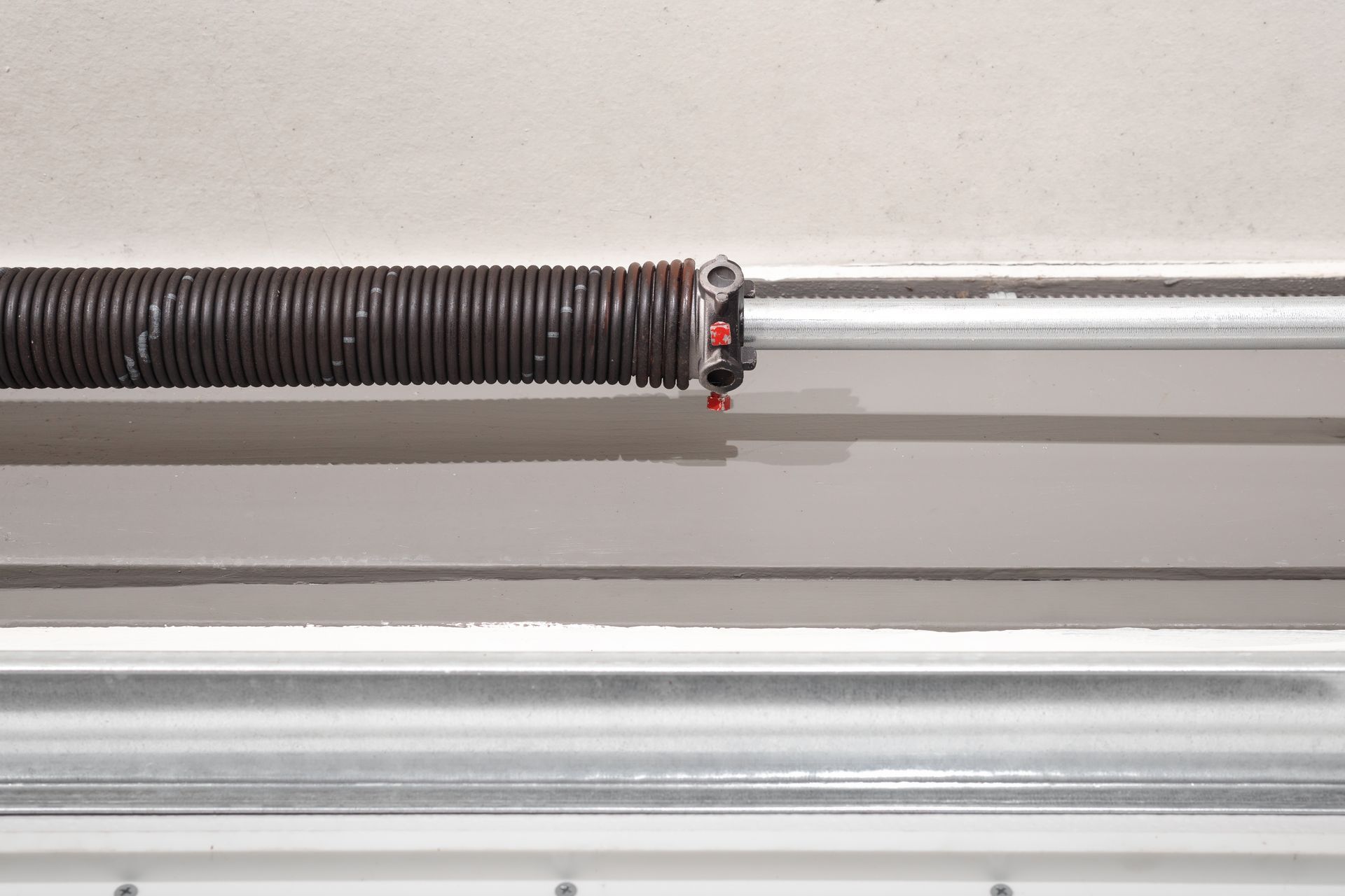 Dark brown torsion spring on a silver bar above a garage door track.