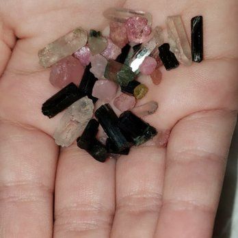 A hand holding assorted small rough crystals and gemstones in black, pink, green, and clear colors