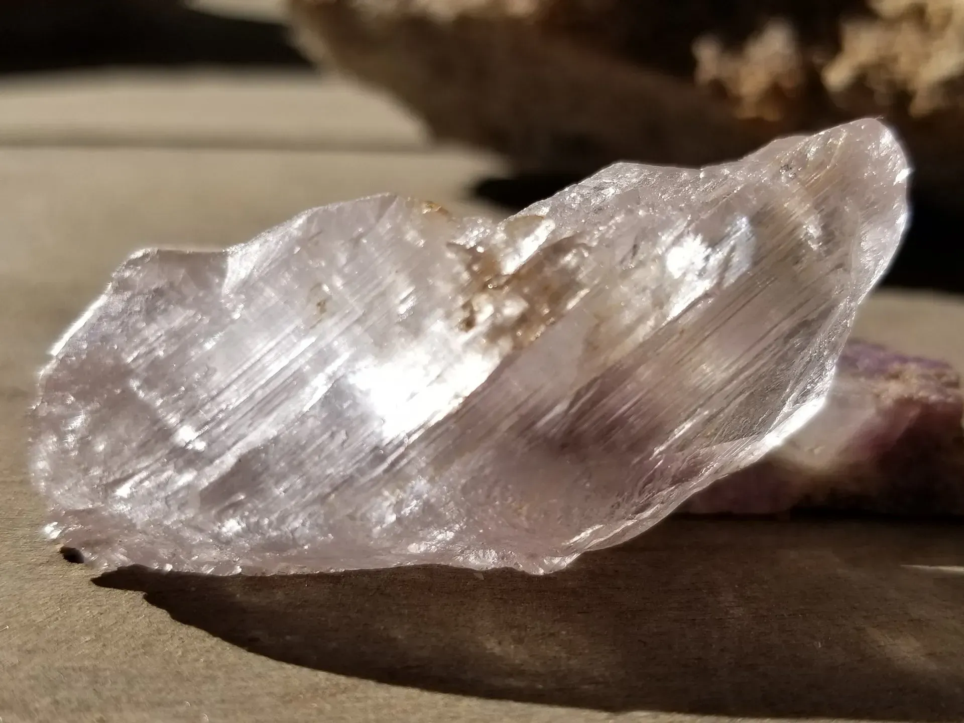 Clear rough crystal mineral on a flat surface, reflecting light with translucent white and brown tones
