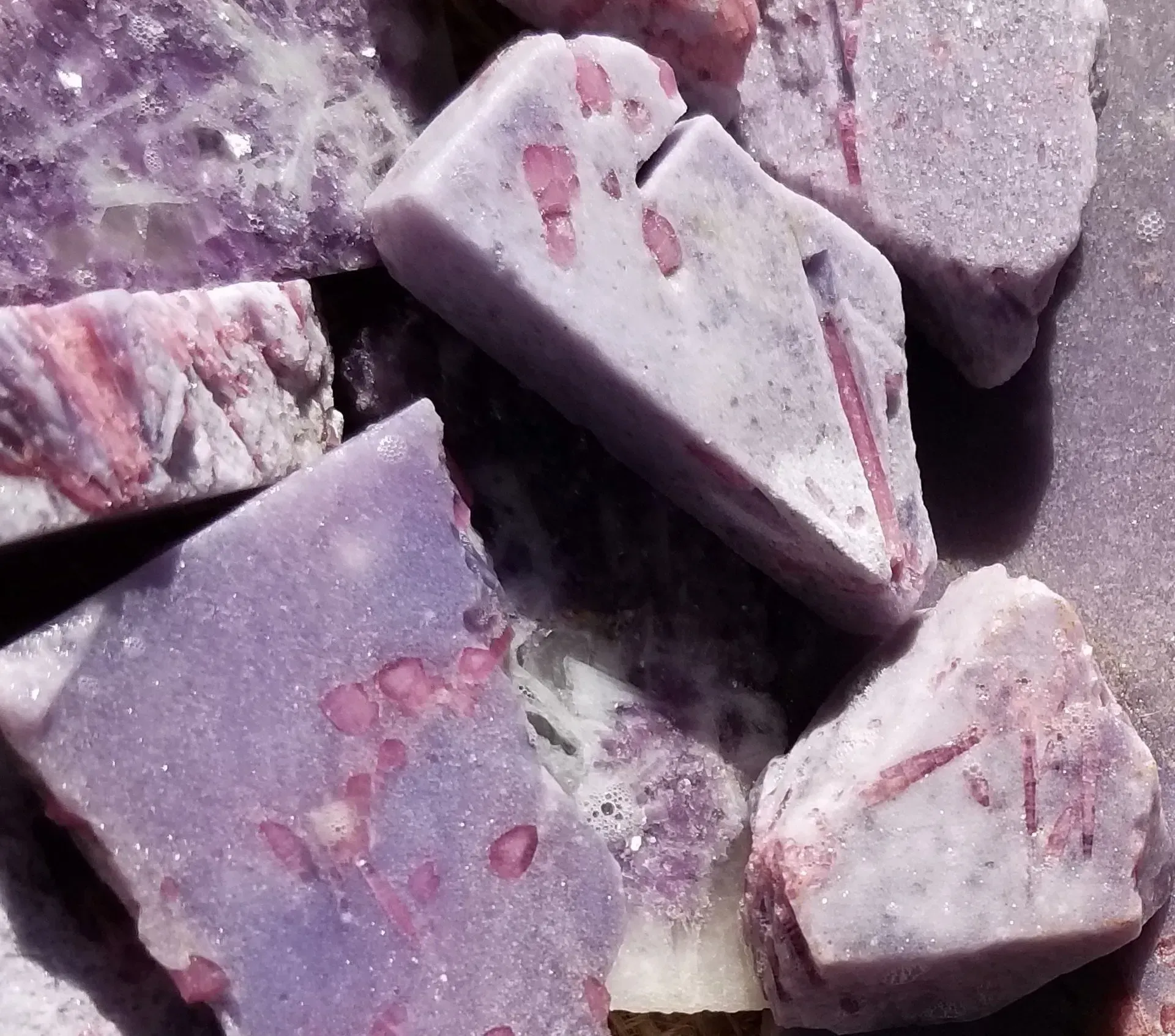 Close-up of rough purple and white crystals with pink speckles on a rocky surface