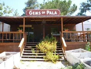 Rustic storefront with sign reading “GEMS OF PALA” and steps leading to the entrance