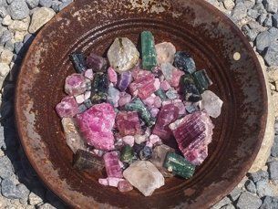 A bowl of mixed colorful crystals and stones, mostly pink, green, and clear, on a textured surface