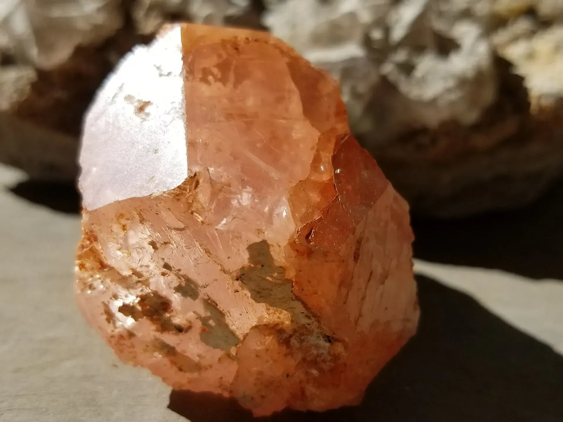 Rough orange-pink crystal with a white reflective patch on a light surface
