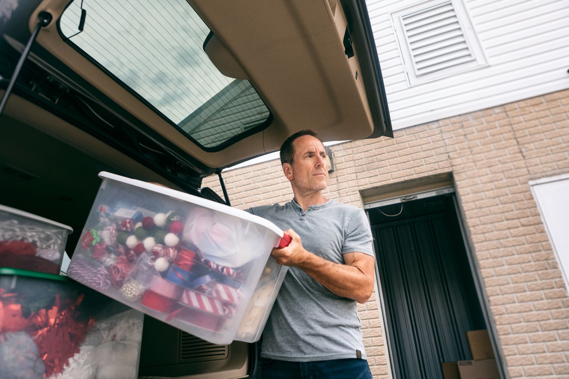 A man carrying a plastic box of Christmas items out of the trunk of his vehicle.