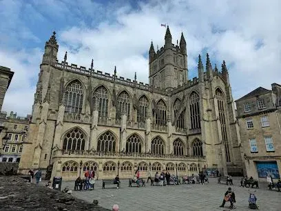 Bath Abbey, a large Gothic church with a tall tower, people in front, cloudy sky.