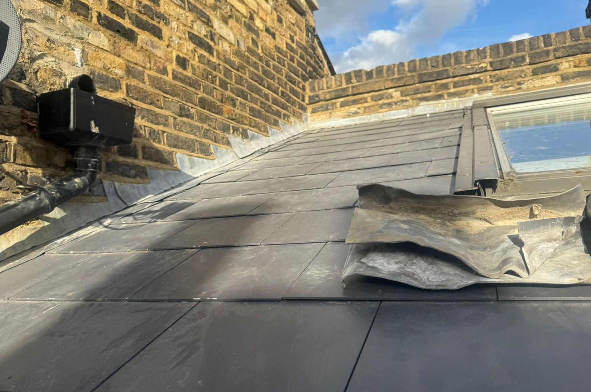 Gray slate roof with damaged flashing against brick building.