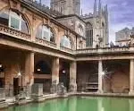 Roman Baths in Bath, England, with green water and a cathedral in the background.