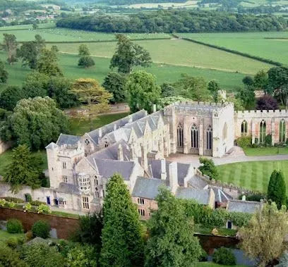 Stone church with multiple gabled roofs, flanked by trees and greenery, in a lush green countryside.