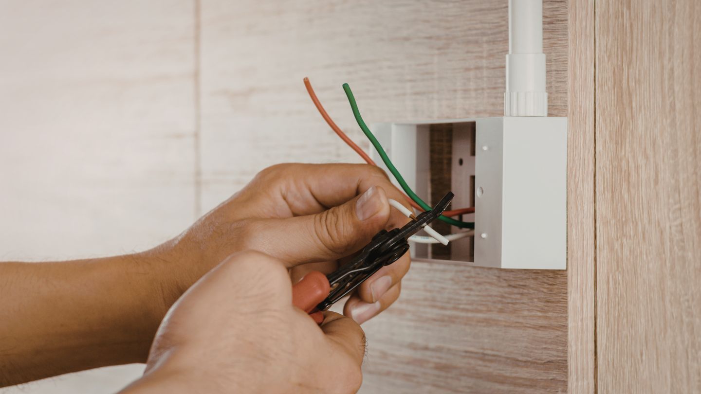 Roofers installing shingles on a house roof. One hammers, the other works in the background. Blue sky overhead.