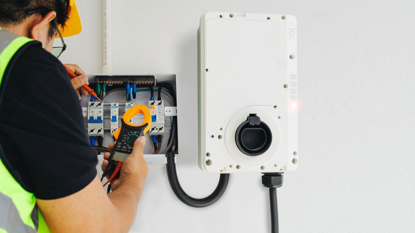 Roofers installing shingles on a house roof. One hammers, the other works in the background. Blue sky overhead.