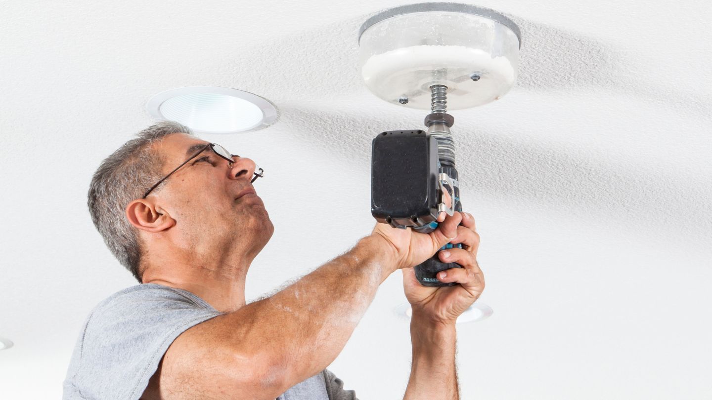 Roofers installing shingles on a house roof. One hammers, the other works in the background. Blue sky overhead.