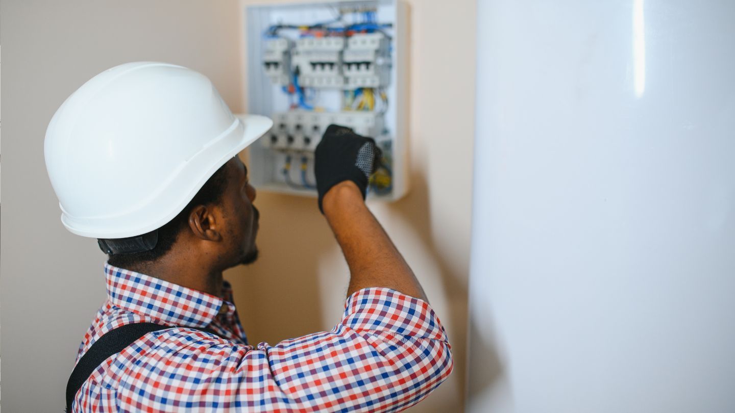 Construction site: partially built house with workers on roof and scaffolding, green field in background.