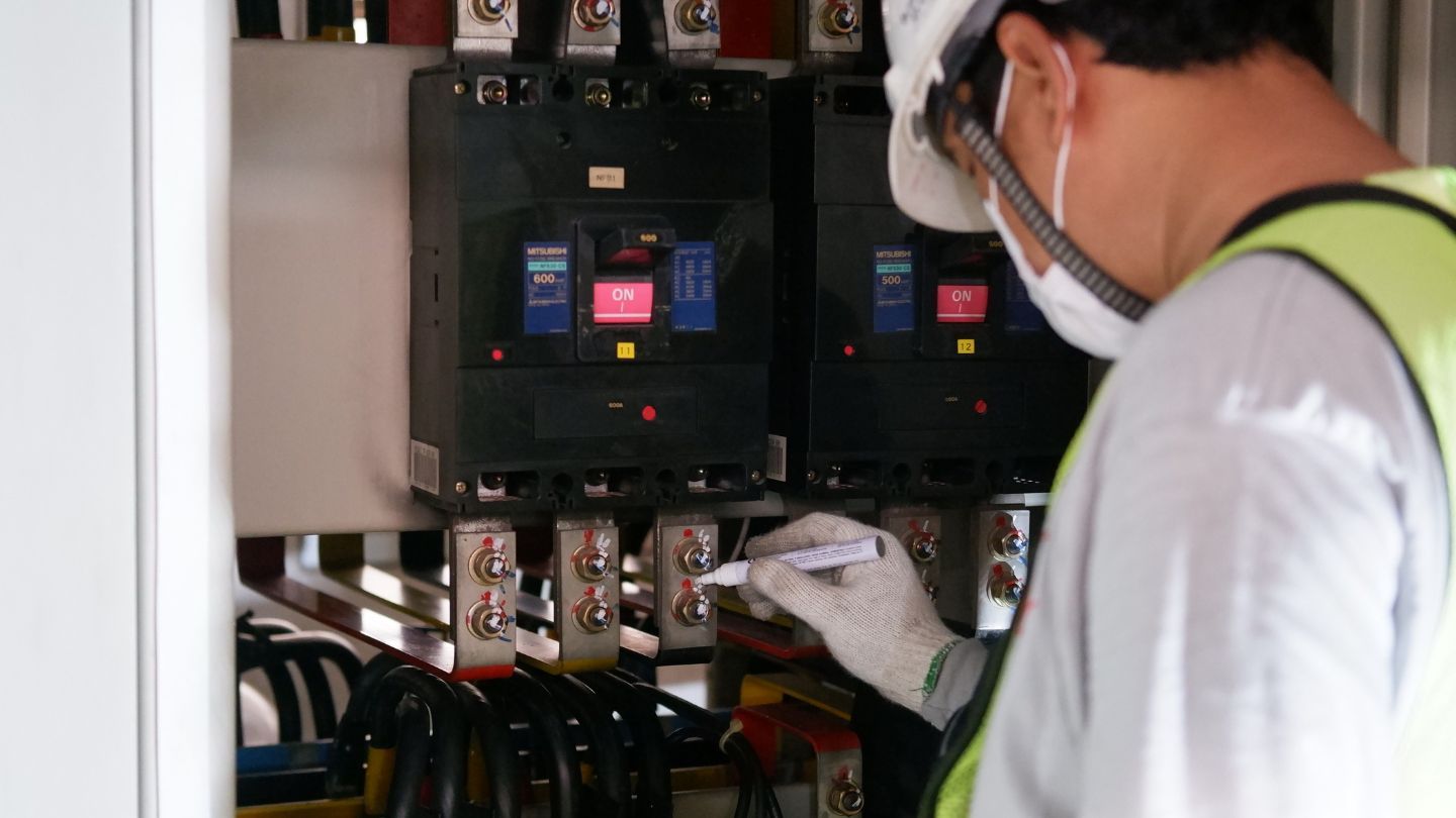 Roofer nailing shingles onto a roof under a bright blue sky.