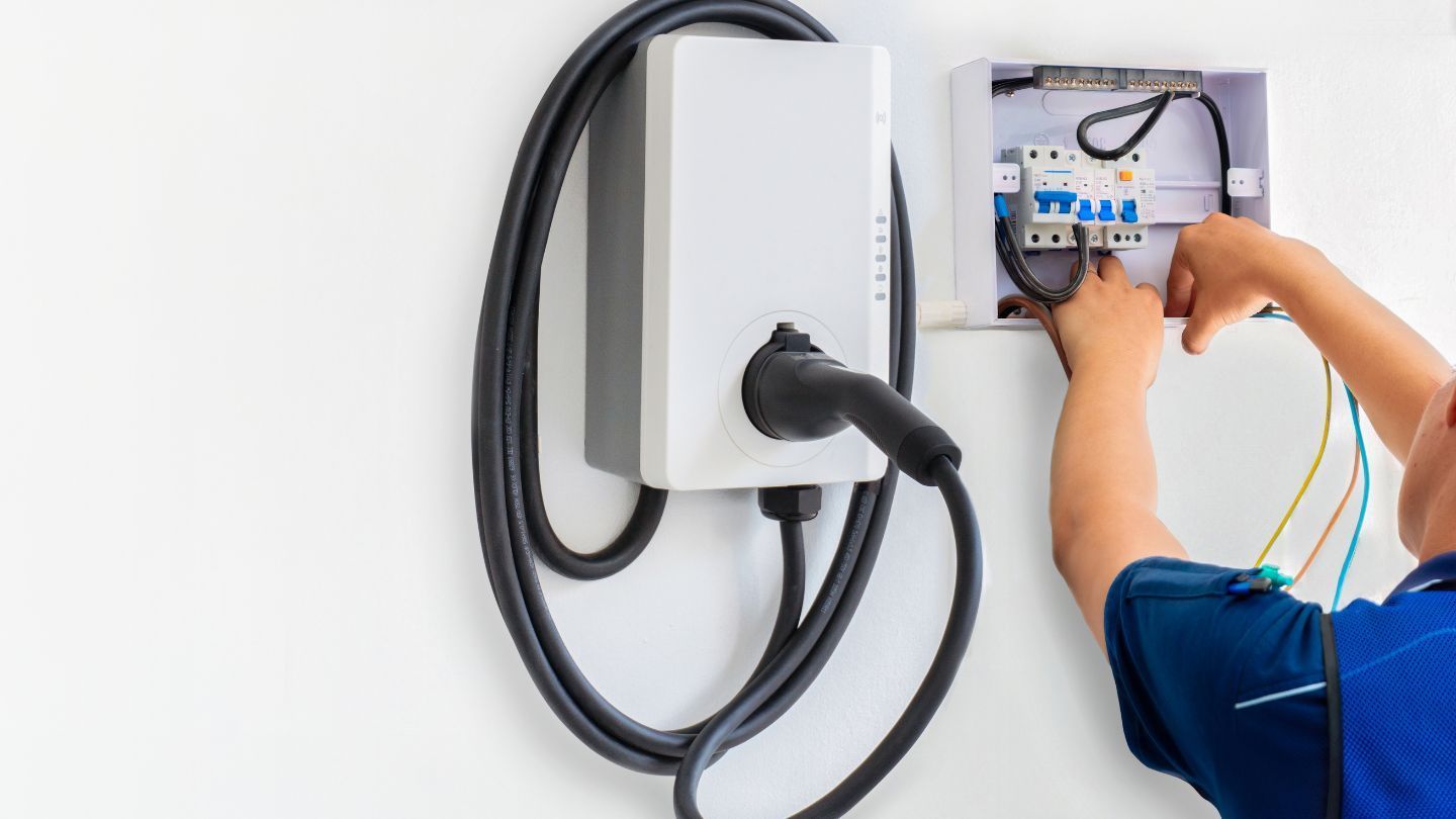 Construction site: partially built house with workers on roof and scaffolding, green field in background.