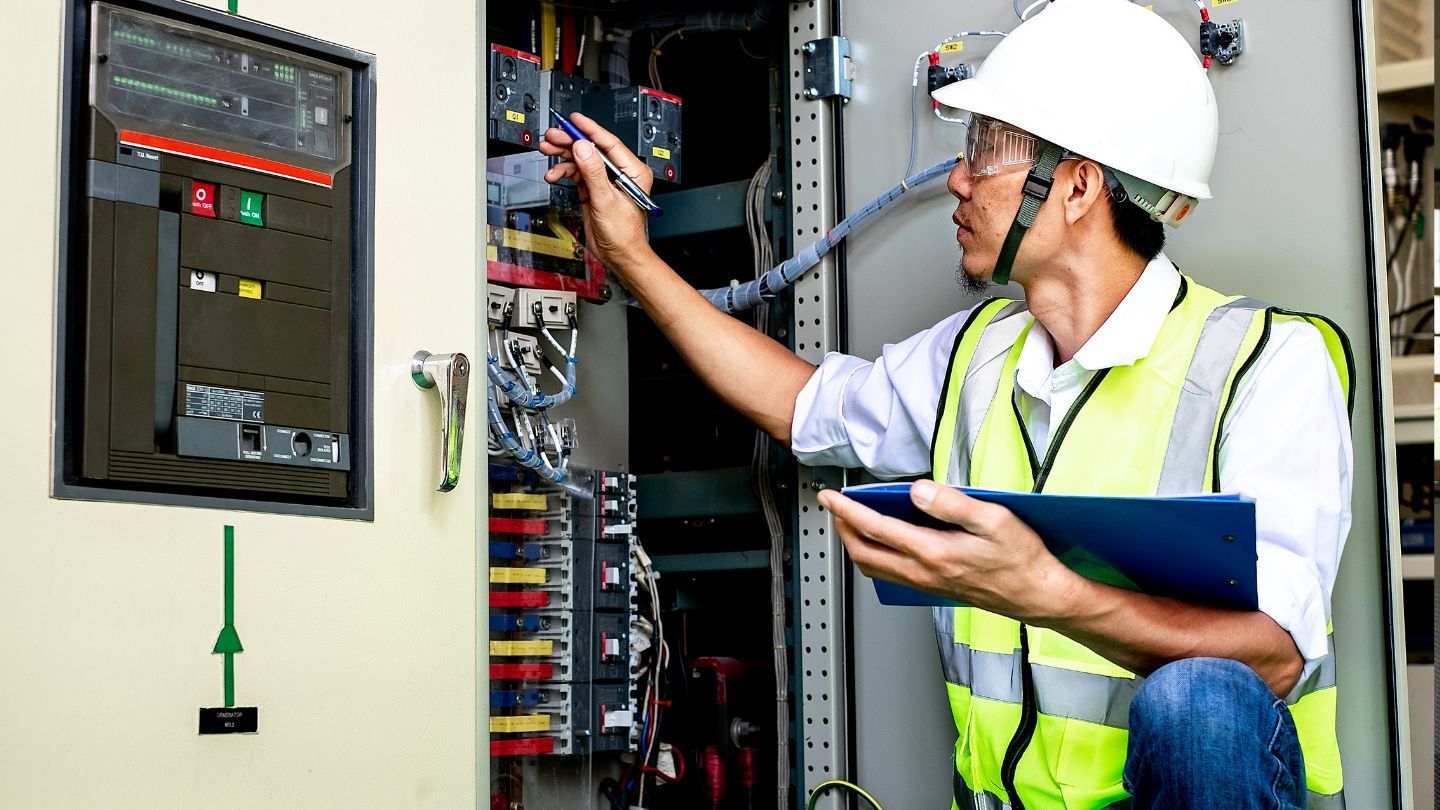 Roofers installing shingles on a house roof. One hammers, the other works in the background. Blue sky overhead.