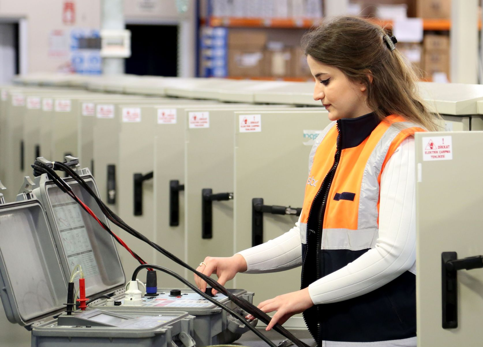 Person operating machinery in a factory, wearing an orange safety vest beside industrial equipment.
