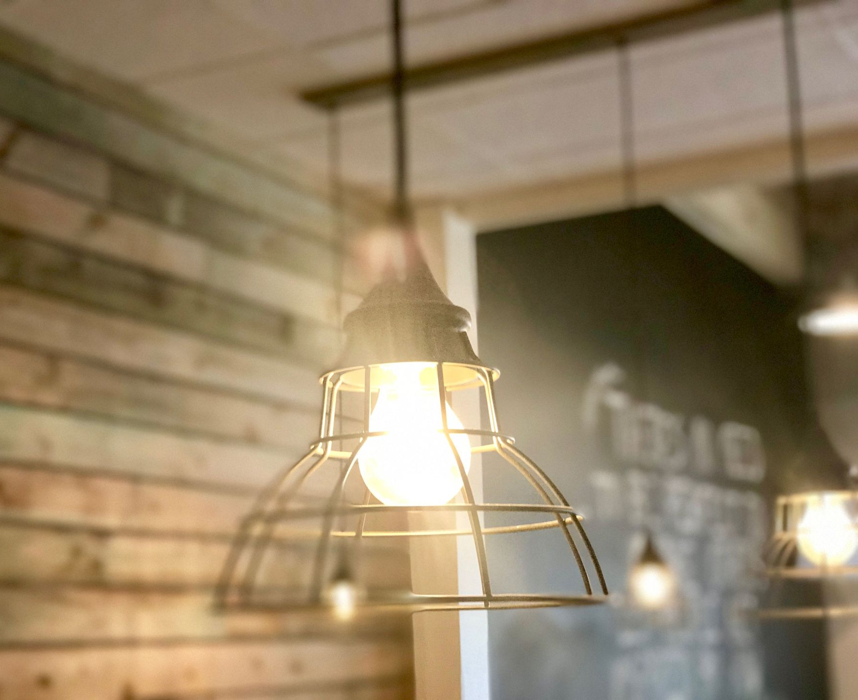 Pendant lights in a rustic wood-paneled room with one bulb glowing in the foreground.