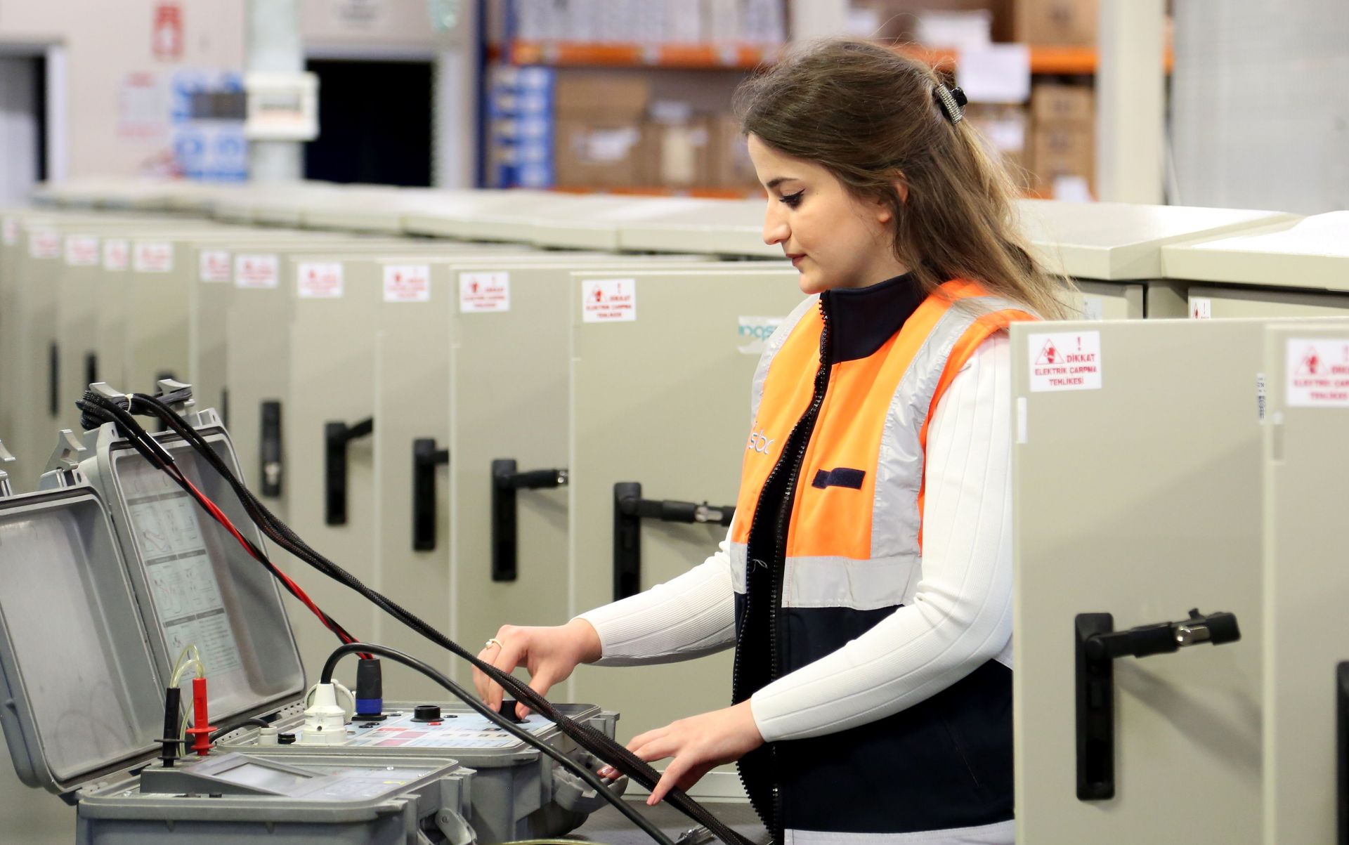 Worker operating a machine in a factory, wearing an orange safety vest.
