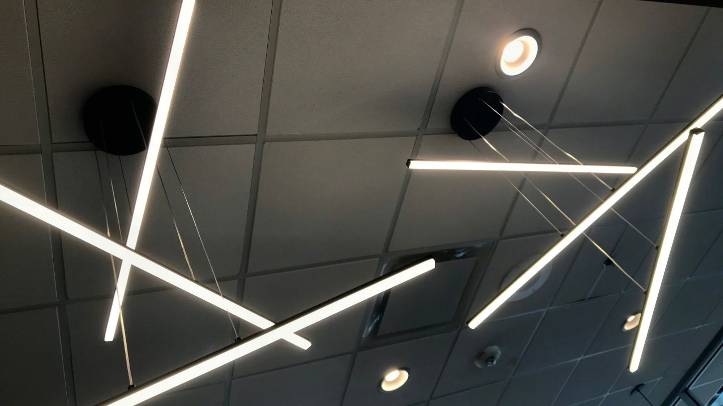 Roofer nailing shingles onto a roof under a bright blue sky.