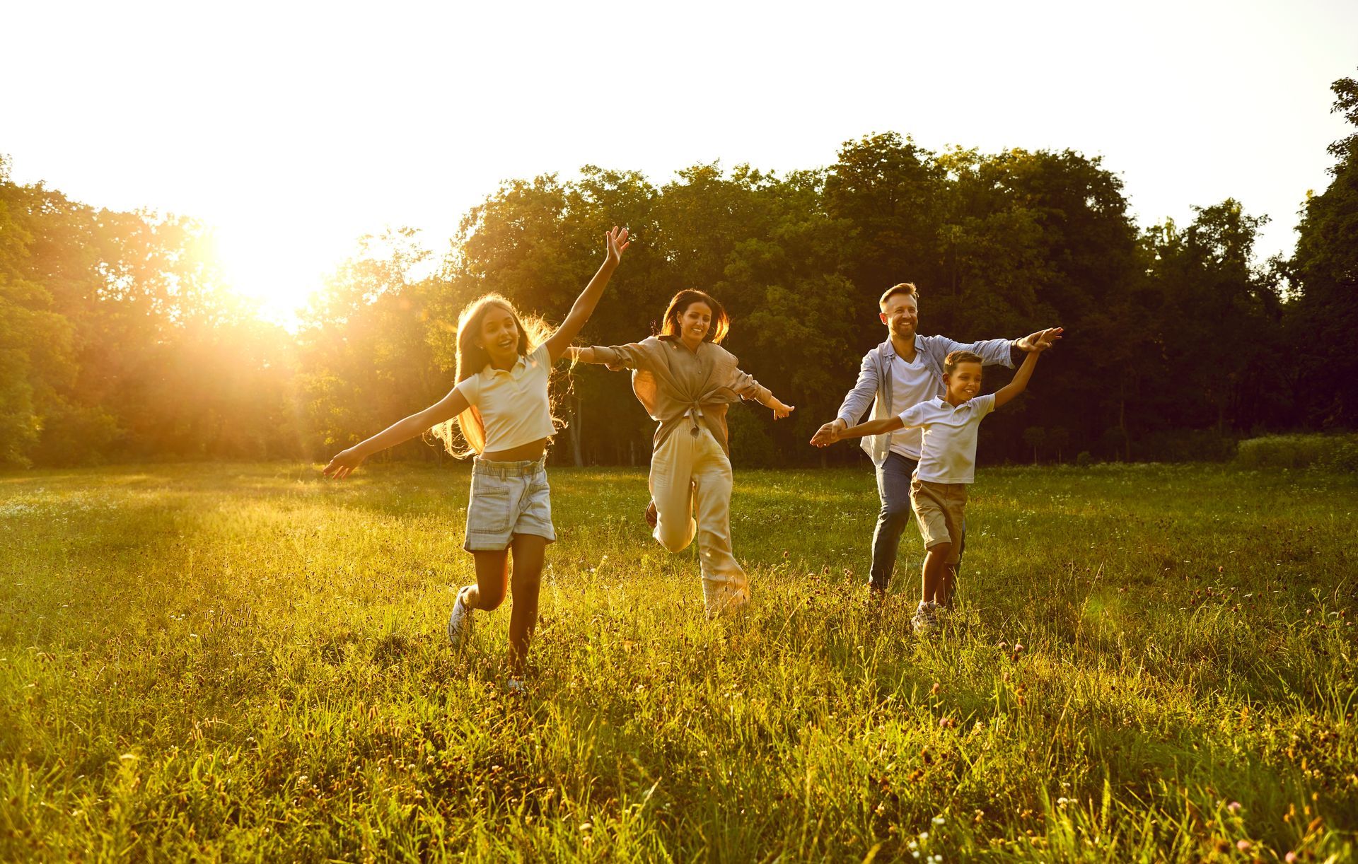 A family is running through a grassy field at sunset.