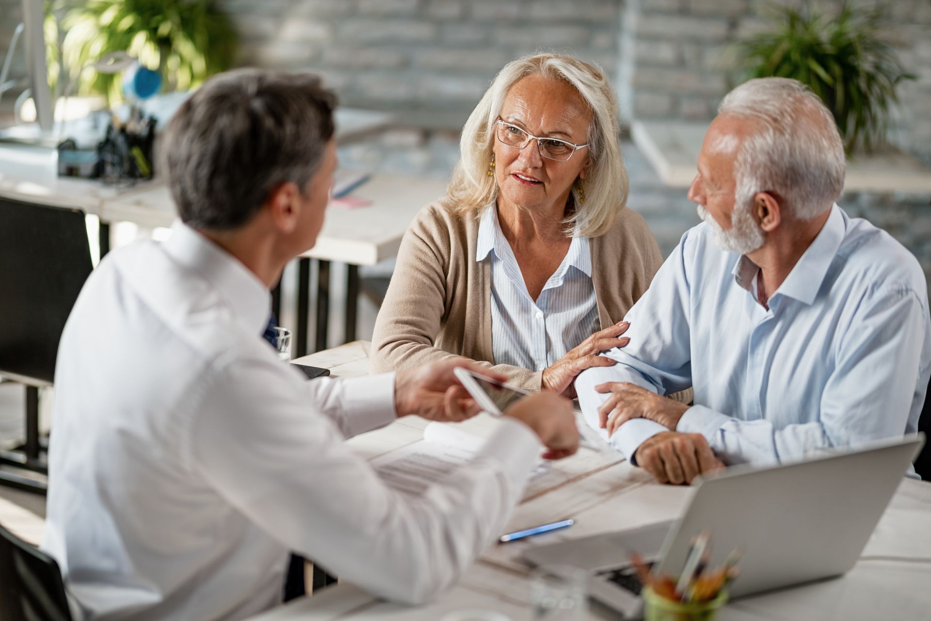 An elderly couple is sitting at a table talking to a man.