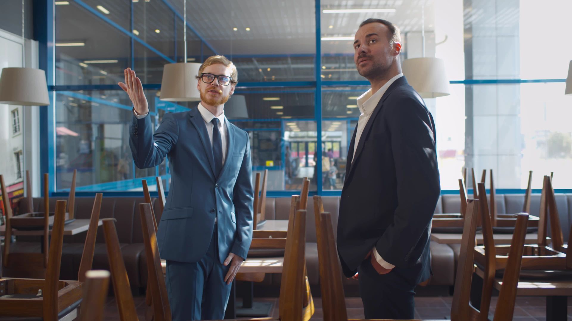 Two men in suits are standing in an empty restaurant.