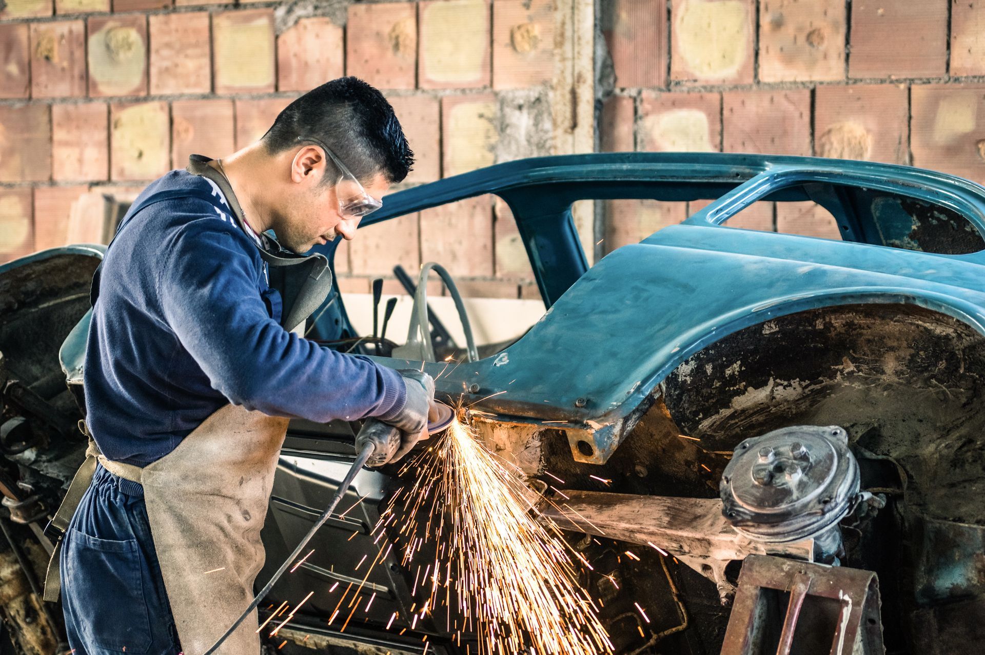 A man is cutting a piece of metal with a grinder in a garage.