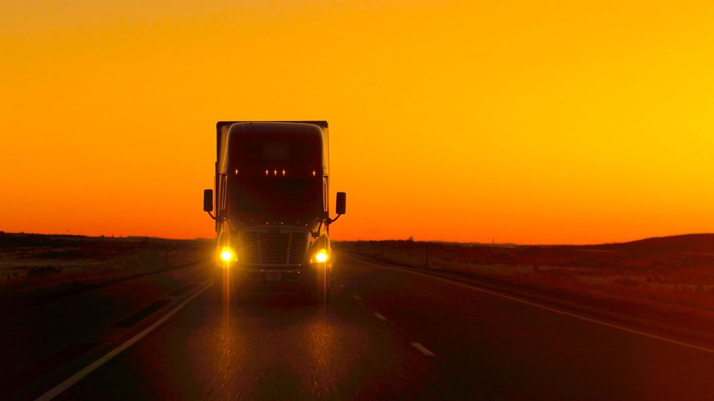 A semi truck is driving down a highway at sunset.