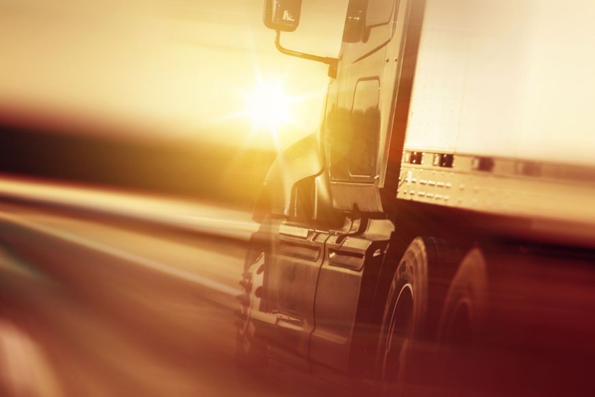 A semi truck is driving down a highway at sunset.