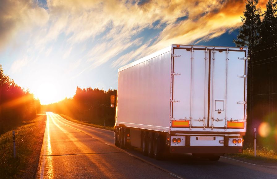 A semi truck is driving down a highway at sunset.
