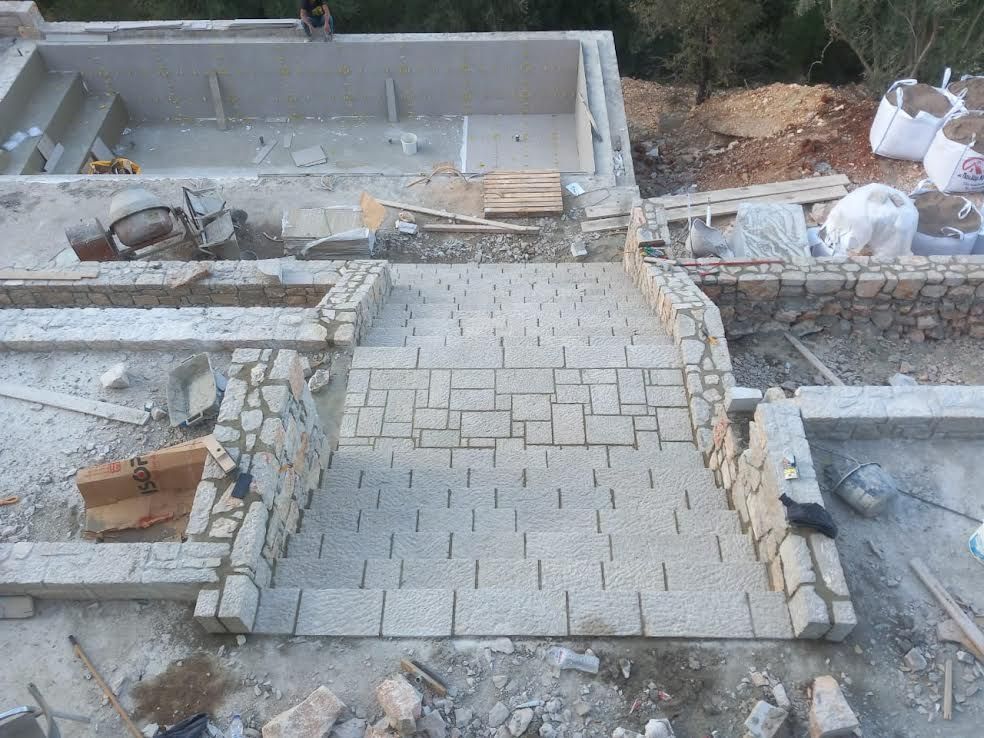 A stone walkway is being built in front of a swimming pool