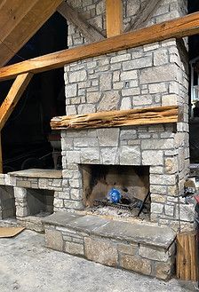 A stone fireplace with a wooden mantle is sitting under a wooden roof.