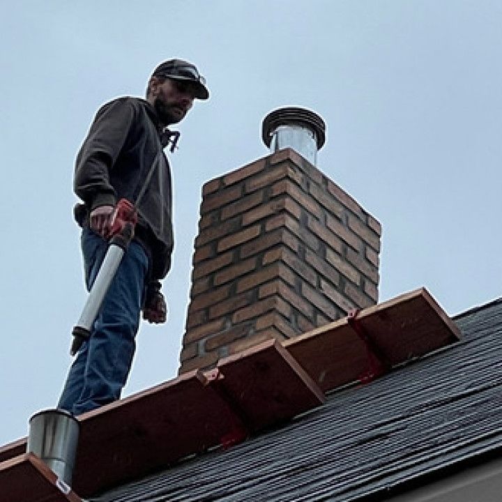 A man is standing on a roof next to a chimney.