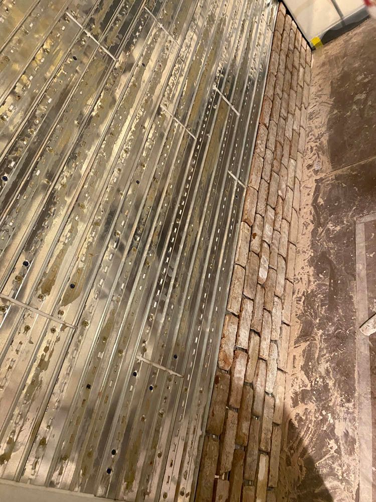 A close up of a metal grate next to a brick wall.