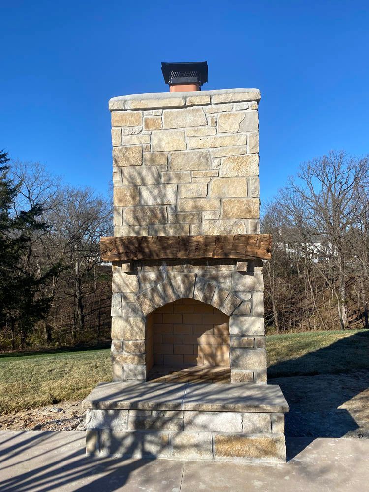 A large stone fireplace is sitting on top of a concrete patio.