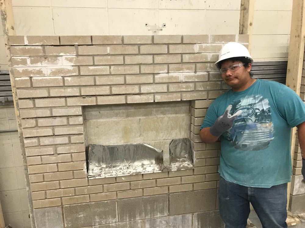 A man wearing a hard hat is standing in front of a brick wall.