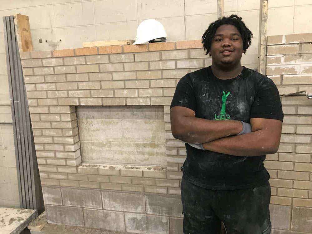 A man is standing in front of a brick wall with his arms crossed.