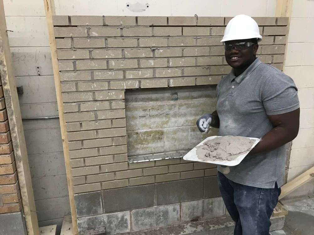 A man is standing in front of a brick wall holding a tray of cement.